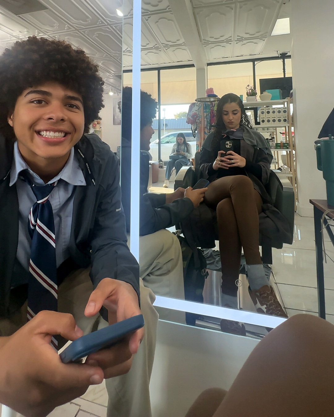 At a salon, Elena getting her hair done with Noah in uniform smiling at the camera.